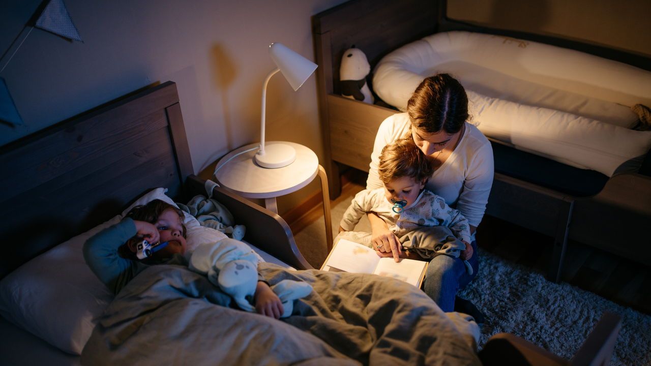 Young mother is reading a book to her two sons for a good night sleep. Night time with reading lamp.